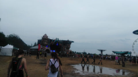 Festival scene with people walking towards a stage on a cloudy day.