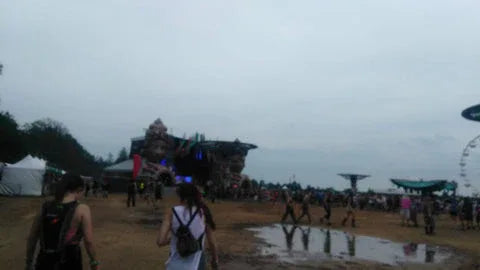 Festival scene with people walking towards a stage on a cloudy day.