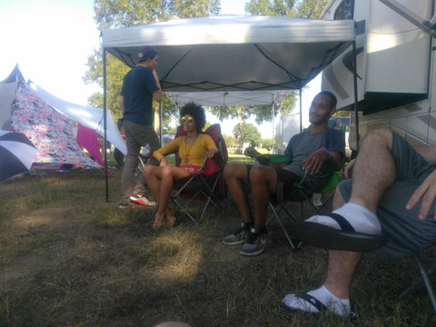 People sitting under a tent at a campsite with tents