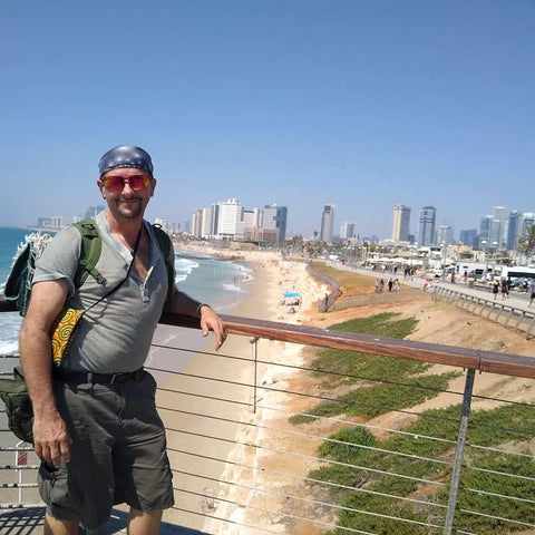 Man with a backpack standing on a balcony overlooking a beach and city