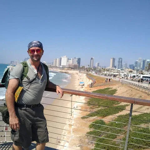 Man with a backpack standing on a balcony overlooking a beach and city