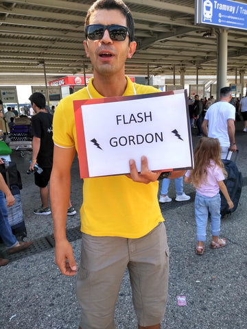 Man holding a sign with 'FLASH GORDON' at a train station.