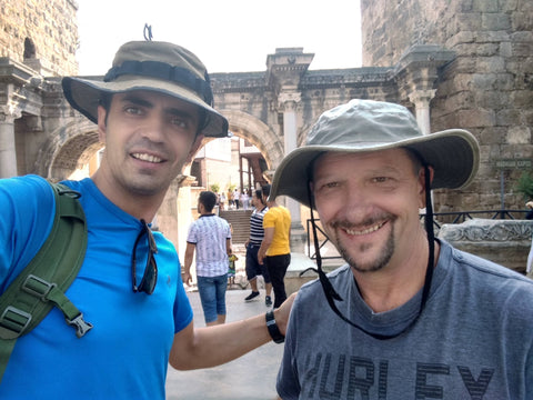 Two men wearing wide-brimmed hats in front of ancient stone architecture.
