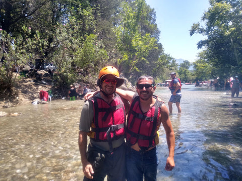 Two people wearing life vests standing in a river with trees