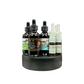A set of dark amber dropper bottles and clear spray vials arranged on a round black stand against a plain white background. The labels show product names including Oil of Elijah, Healing & Anointing Oil, and V-Ghets.
