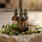 A set of amber glass dropper bottles and clear spray bottles with black caps, including a large central bottle labeled 'Oil of Elijah Healing & Anointing Oil' and smaller bottles labeled 'V-Shield' and 'V-Shield Nasal Drop'.