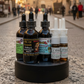 A set of herbal oil dropper bottles and nasal spray vials arranged on a round black stand against a plain white background. The bottles are dark amber glass with black caps, and the vials on the right have clear caps and white labels.